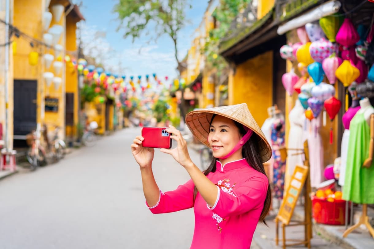 Femme en costume traditionnel se prenant en photo avec un smartphone à Hoi An, Vietnam.